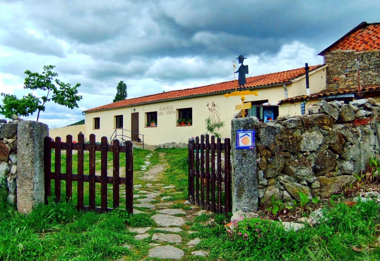 Alba-Soraya hostel with its wooden gate and a pilgrim marker by the path, stage towards La Calzada de Béjar