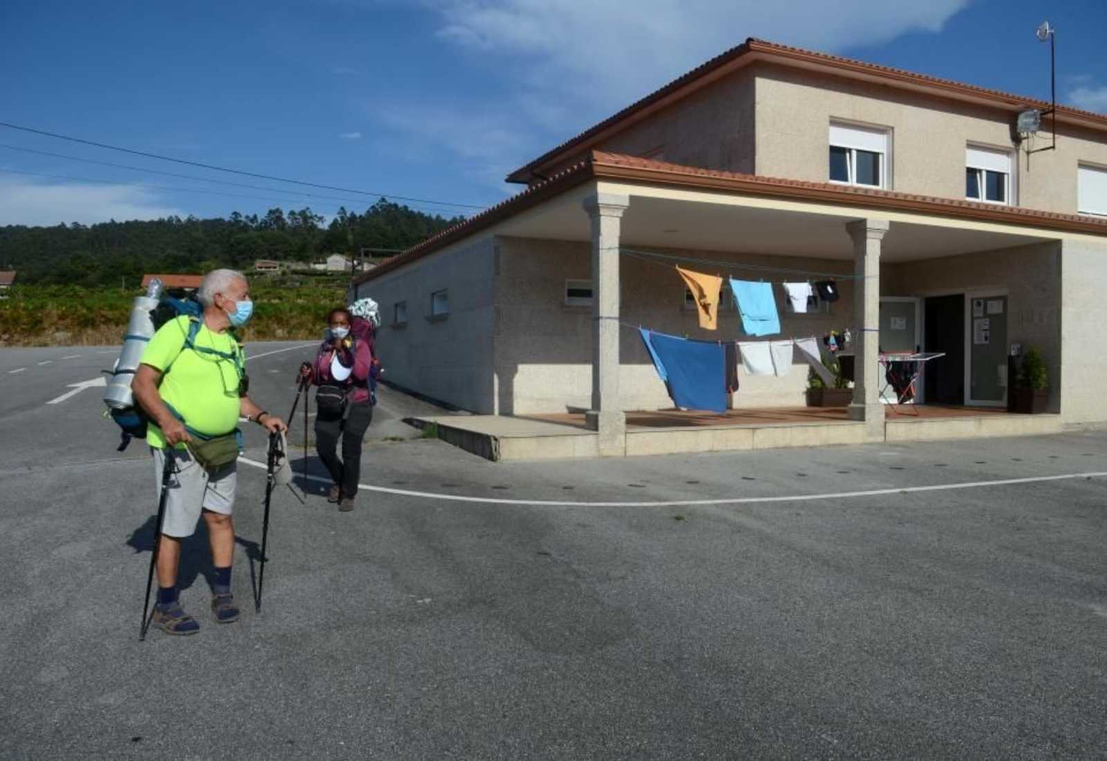 Deux pèlerins avec sac et bâtons marchent devant un gîte au linge étendu, de A Armenteira à Vilanova de Arousa