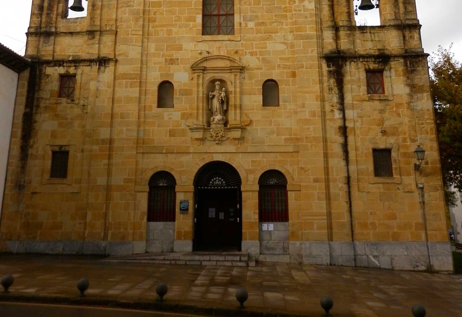 Facciata in pietra dorata con due campanili e una nicchia con statua religiosa nella tappa da Deba a Markina del Cammino del Nord.