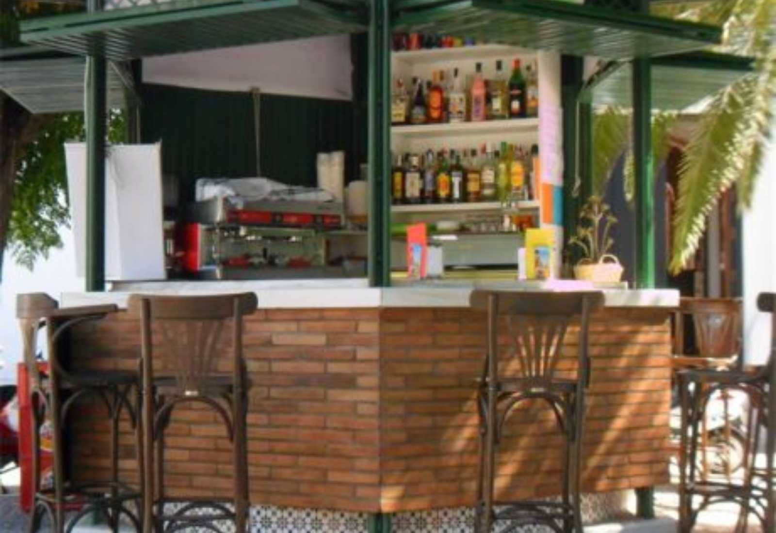 Bar del albergue con barra de ladrillo, taburetes de madera y estantería de botellas en la etapa De Zafra a Villafranca de los Barros.