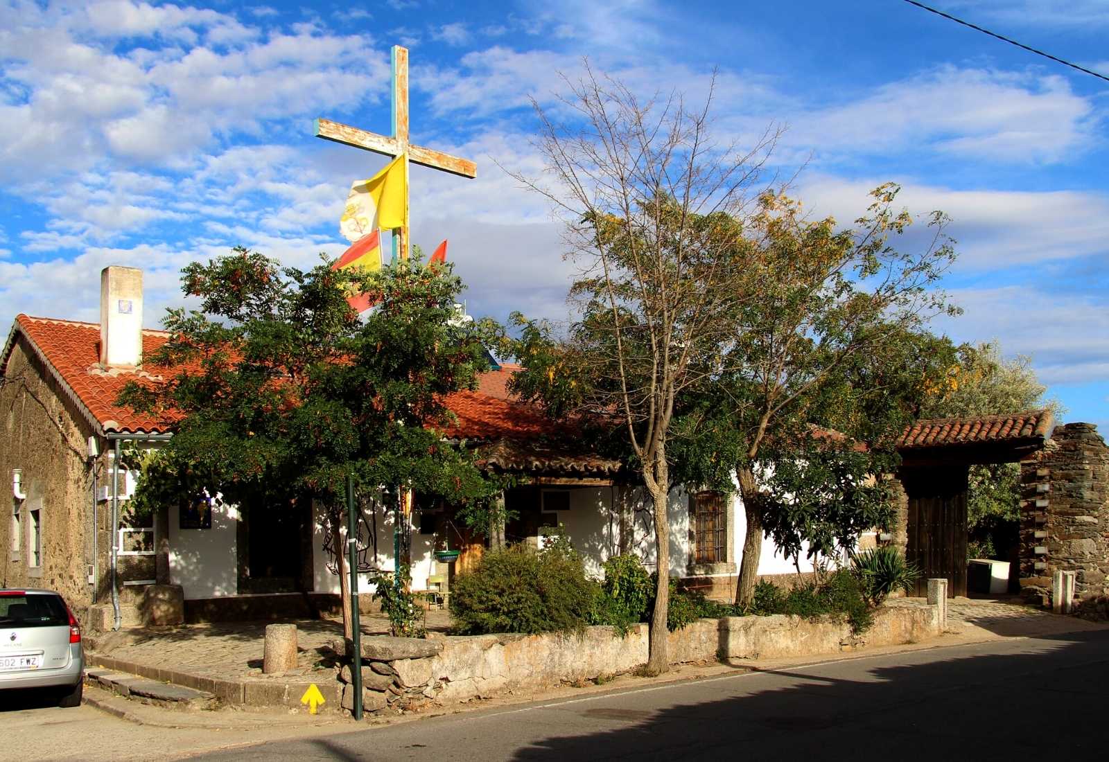 Pilgrim hostel in a whitewashed house with a large wooden cross and yellow arrow in Fuenterroble de Salvatierra.