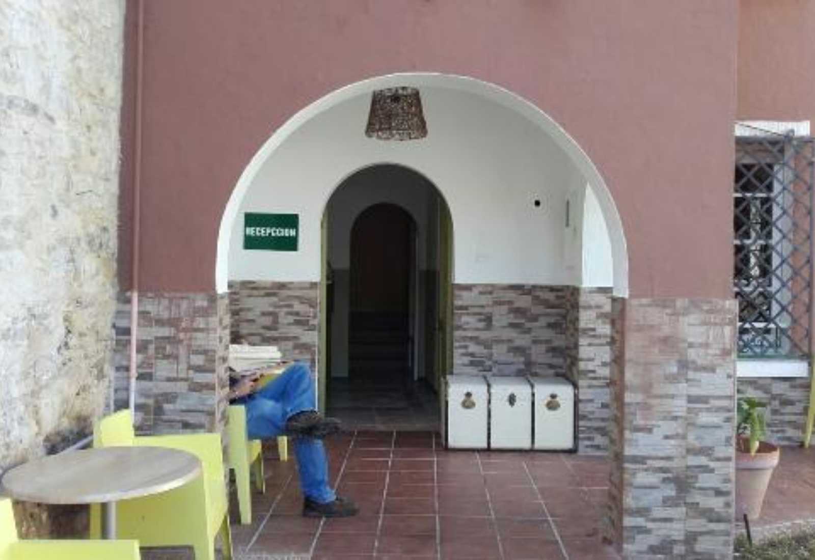 Espace d'accueil couvert d'une auberge avec une arche, un pèlerin au repos et des malles blanches sur l'étape de Gijón à Avilés du Chemin du Nord.