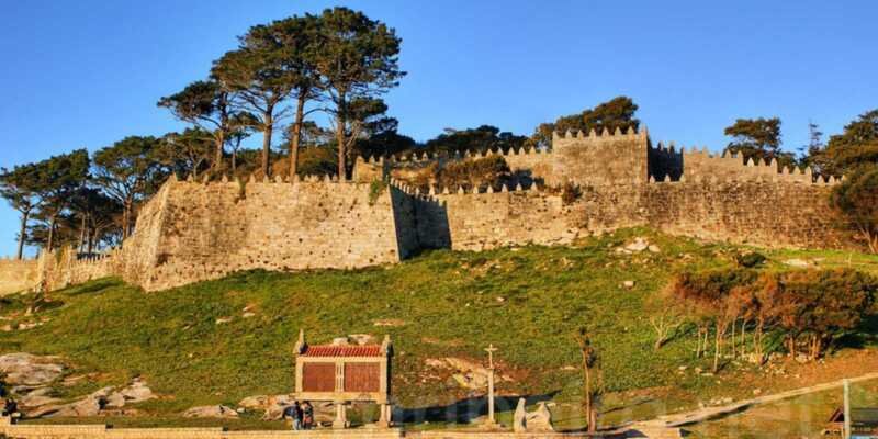 Muralhas ameadas da fortaleza de Baiona com um espigueiro e um cruzeiro na etapa de Vila Praia de Ancora a Baiona do Caminho Português