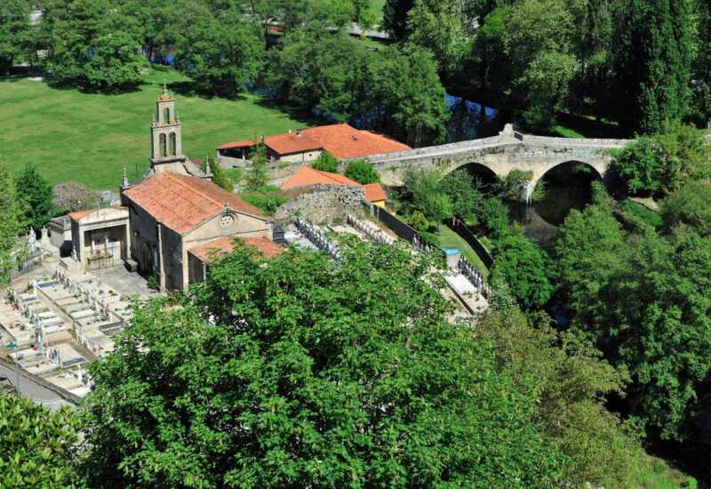 Aldea con iglesia y puente medieval de piedra sobre el río vista desde lo alto, en la etapa de Laza a Xunqueira de Ambía.