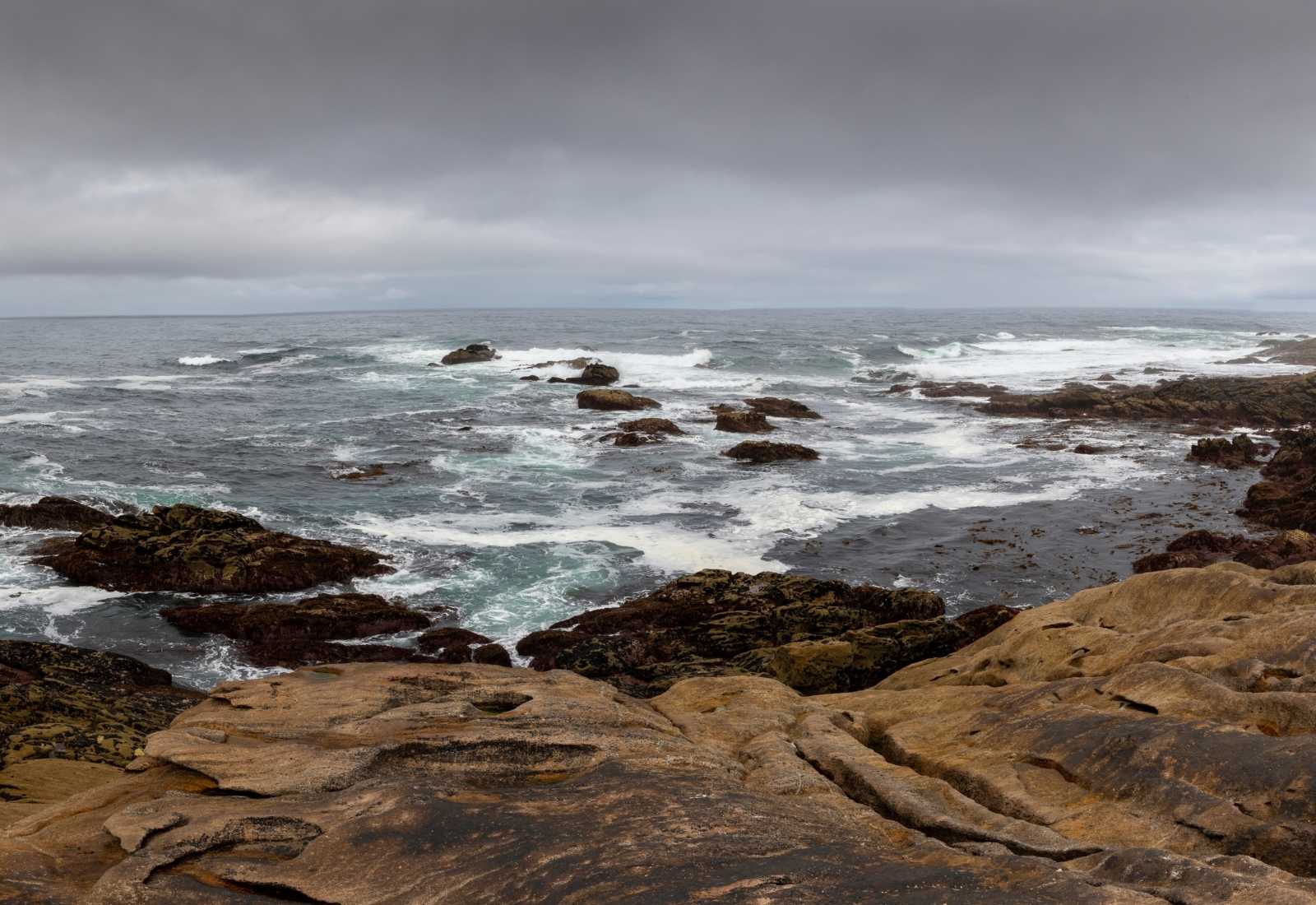Costa rocosa del Atlántico con olas rompiendo bajo un cielo gris en la etapa de Laxe a Arou del Camino dos Faros