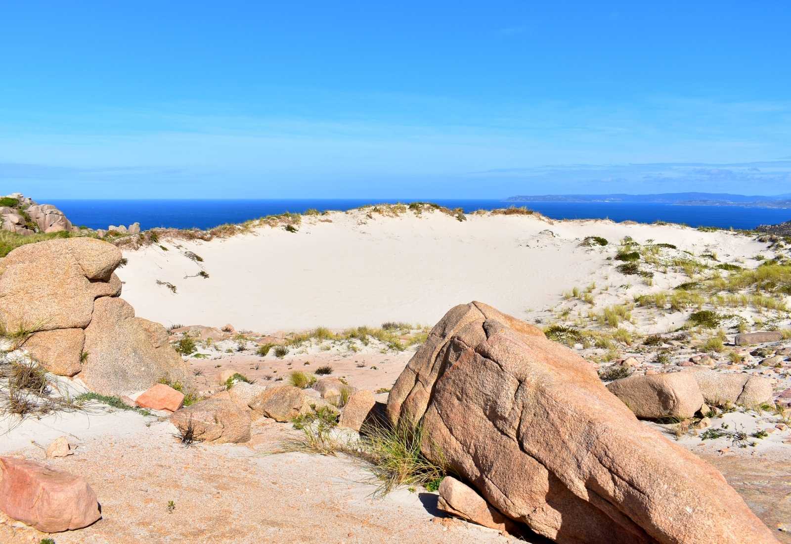 Duna blanca entre rocas de granito con el mar al fondo en la etapa de Arou a Camariñas del Camino dos Faros