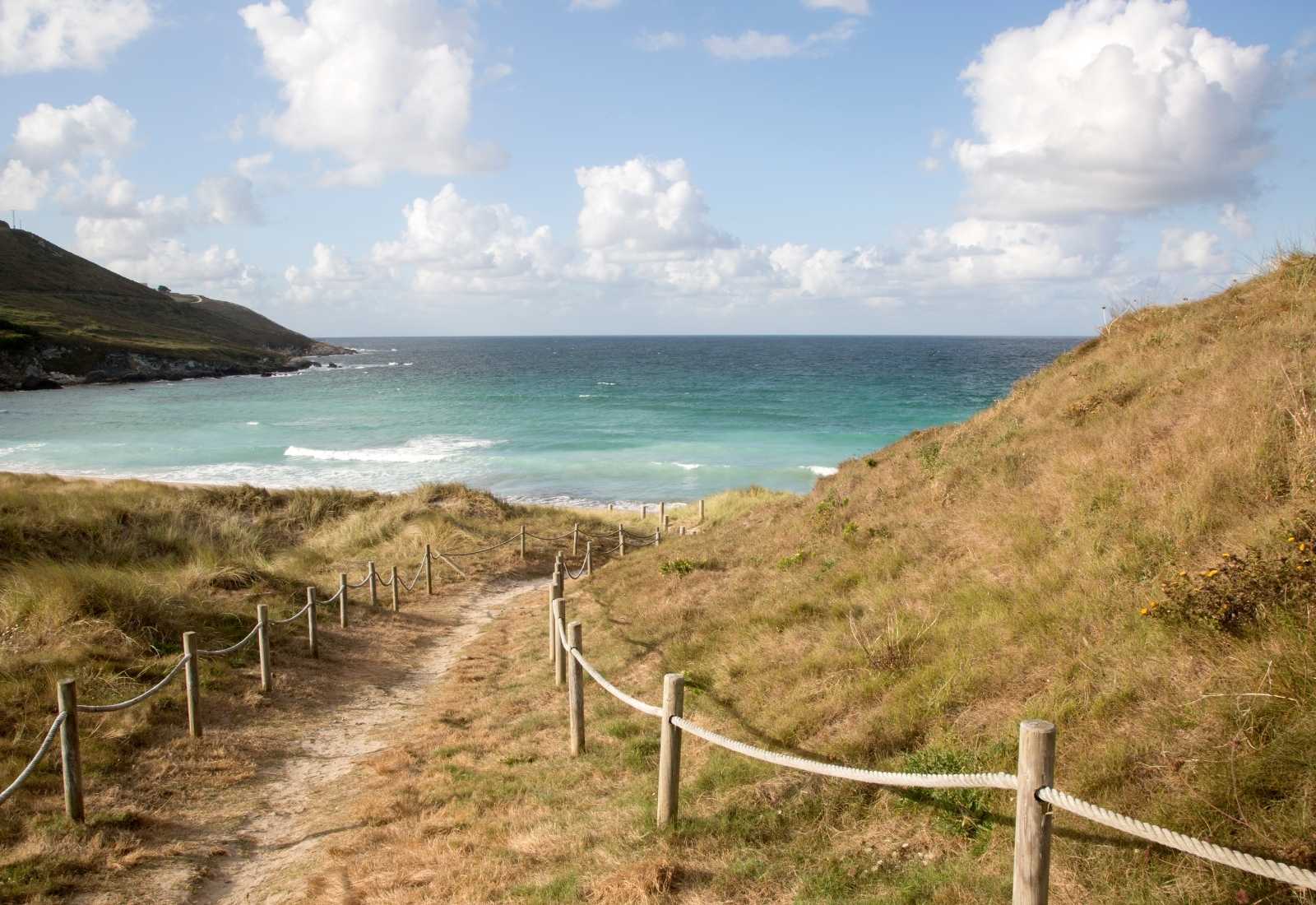 Sendero de cuerdas que baja entre dunas hacia una playa turquesa a la llegada a Malpica de Bergantiños en el Camino dos Faros