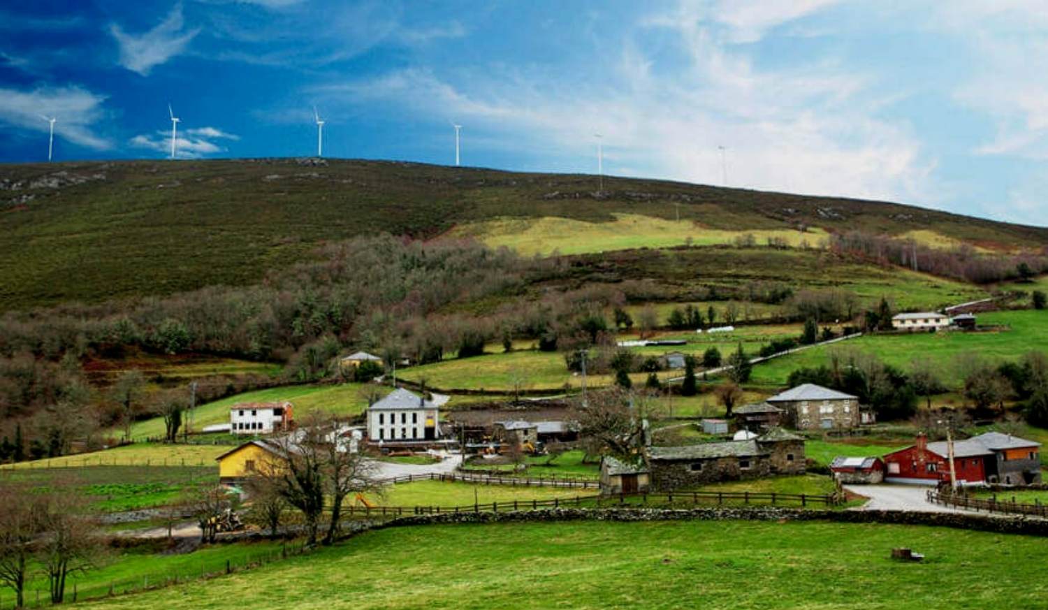 A aldeia de La Mesa na encosta com aerogeradores no cume, início da etapa de La Mesa a Grandas de Salime do Caminho Primitivo
