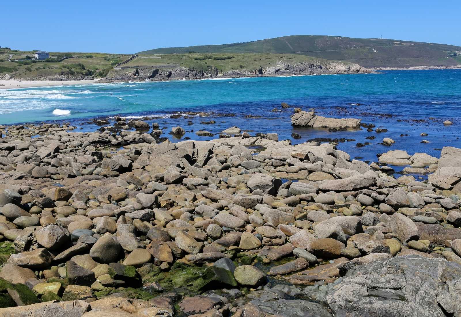 Costa de cantos rodados y mar turquesa con la playa al fondo a la llegada a Malpica de Bergantiños en el Camino dos Faros