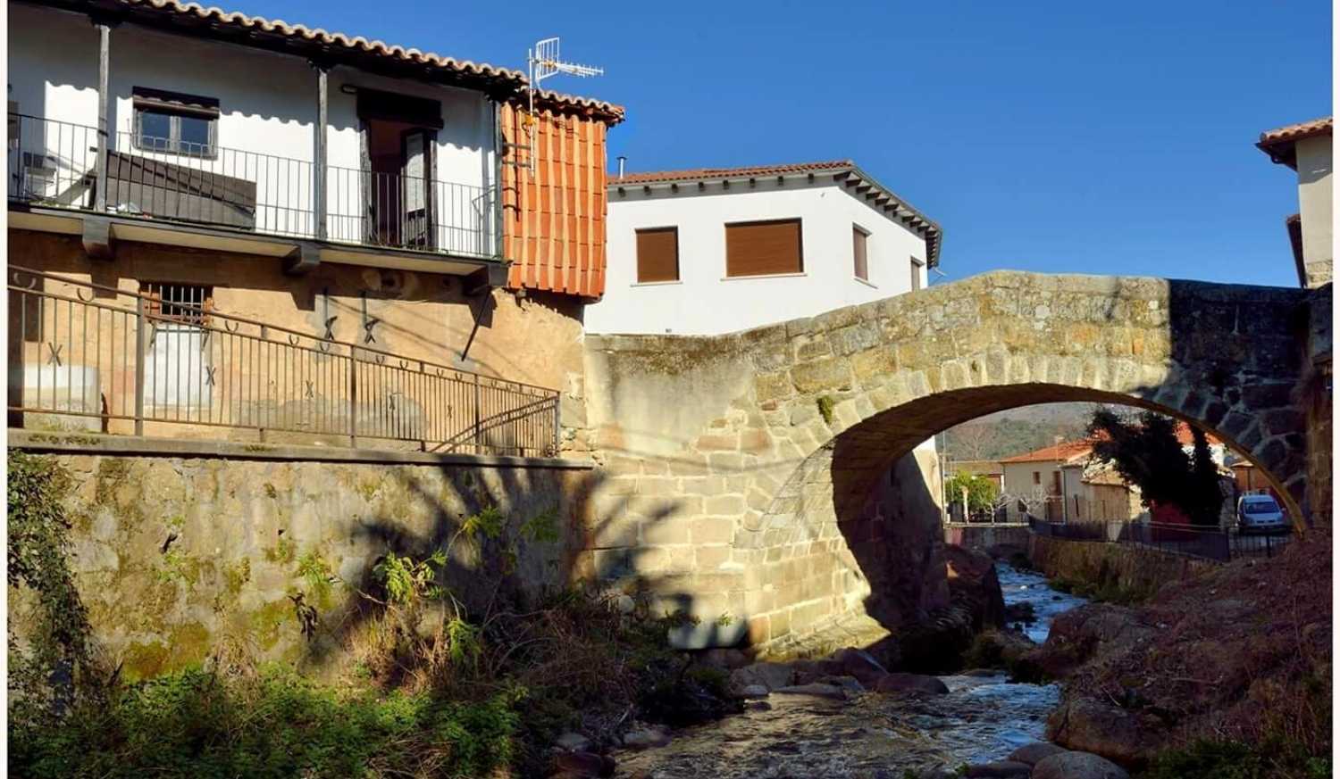 Old stone bridge over a stream and balconied houses in Aldeanueva del Camino, start of the stage to La Calzada de Béjar