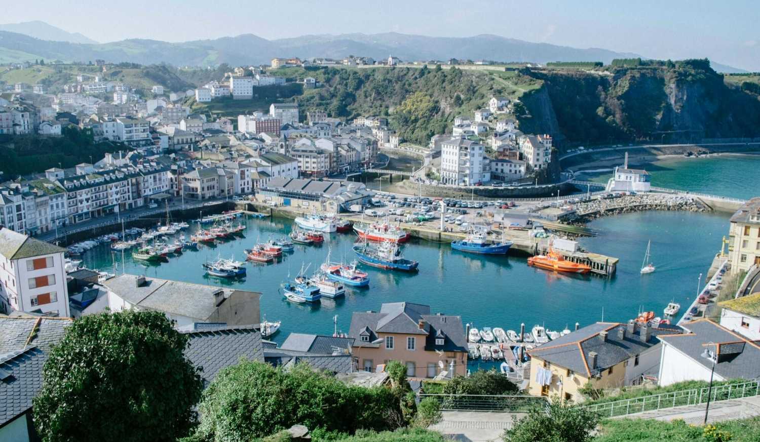 Vista elevada do porto e da vila de Luarca com barcos coloridos e casas brancas, meta da etapa do Caminho do Norte desde Cadavedo.