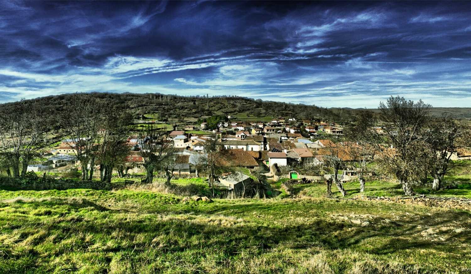 View of La Calzada de Béjar village among the hills with red rooftops under a cloudy sky, stage from Aldeanueva del Camino