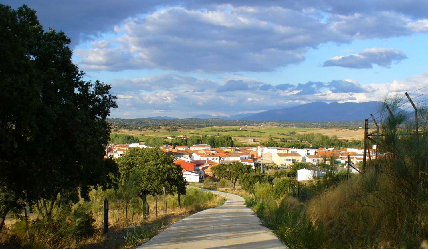 View of Carcaboso village from the path, with red roofs and mountains behind, stage to Aldeanueva del Camino.