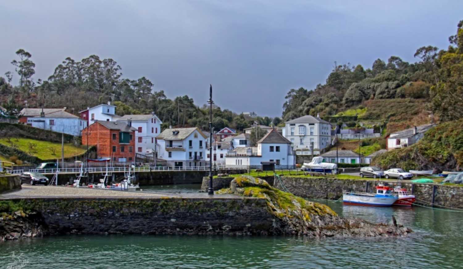 Petit port de pêche aux barques amarrées et maisons sur les coteaux verts sur l'étape de La Caridad à Ribadeo du Chemin du Nord.