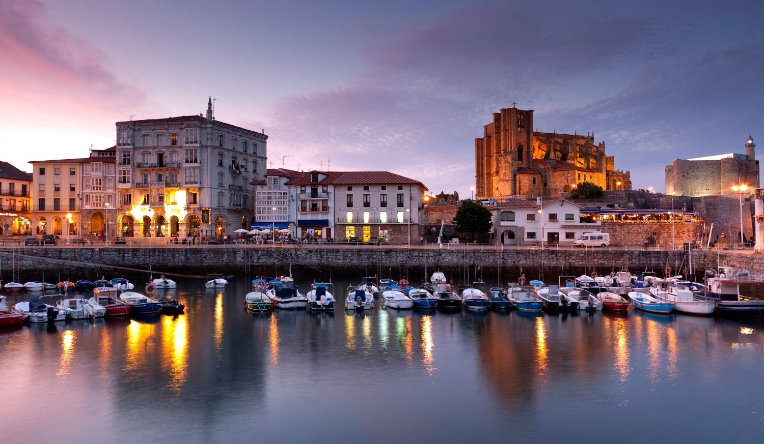 Paese di mare con il porto e una grande chiesa al tramonto nella tappa da Portugalete a Castro Urdiales del Cammino del Nord.