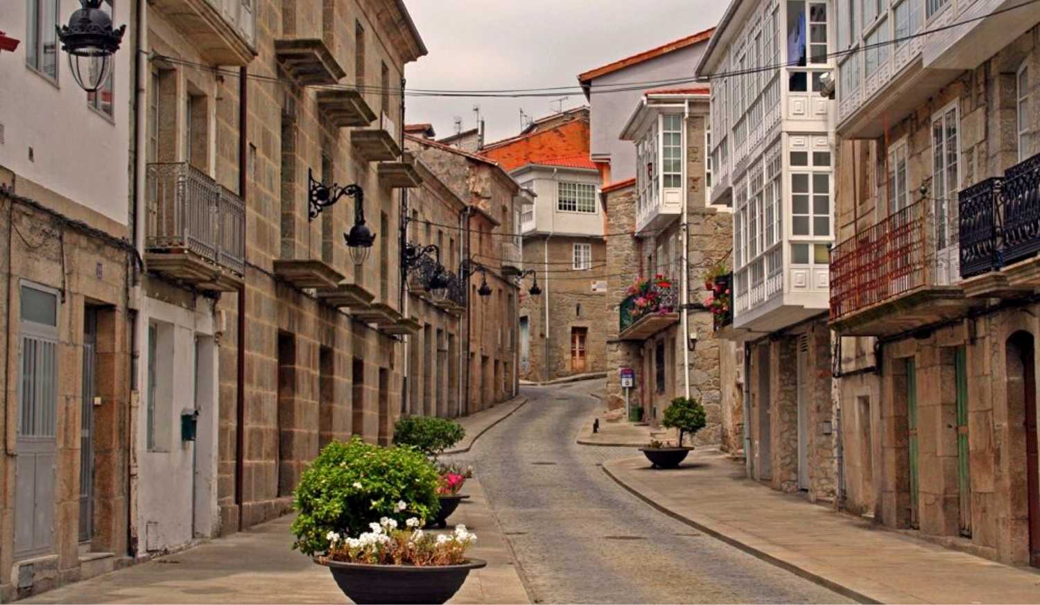 Via lastricata del centro storico con case in pietra, gallerie vetrate e fioriere, tappa da Monforte de Lemos a Chantada.
