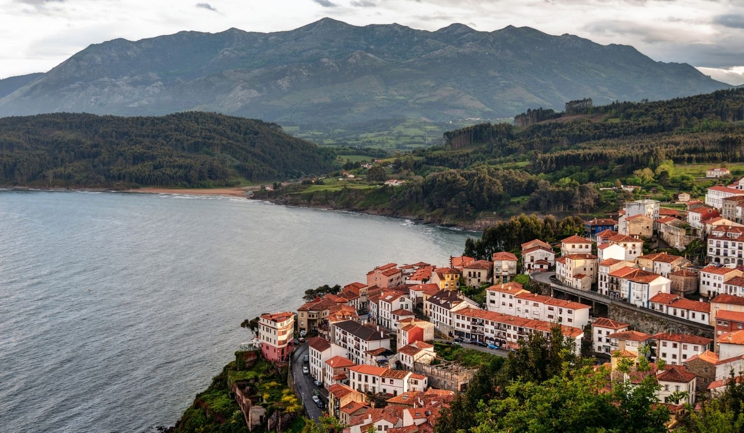 Seaside village of red-roofed houses perched above the sea between green mountains on the Ribadesella to Colunga stage of the Camino del Norte