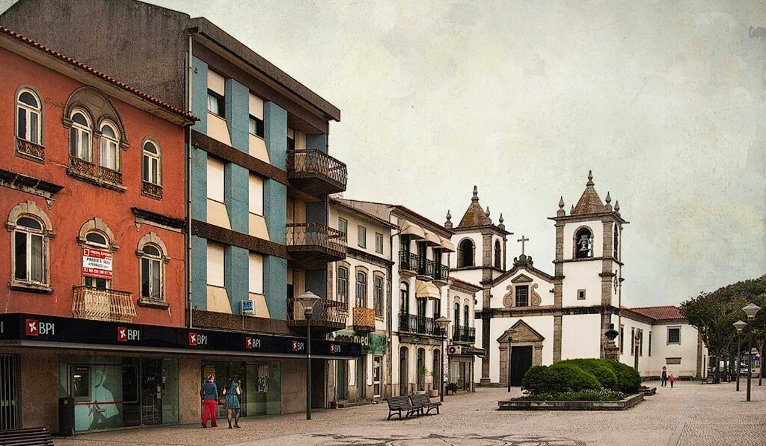 Praça empedrada da vila com uma igreja de duas torres e casas coloridas na etapa de Esposende a Viana do Castelo do Caminho Português.