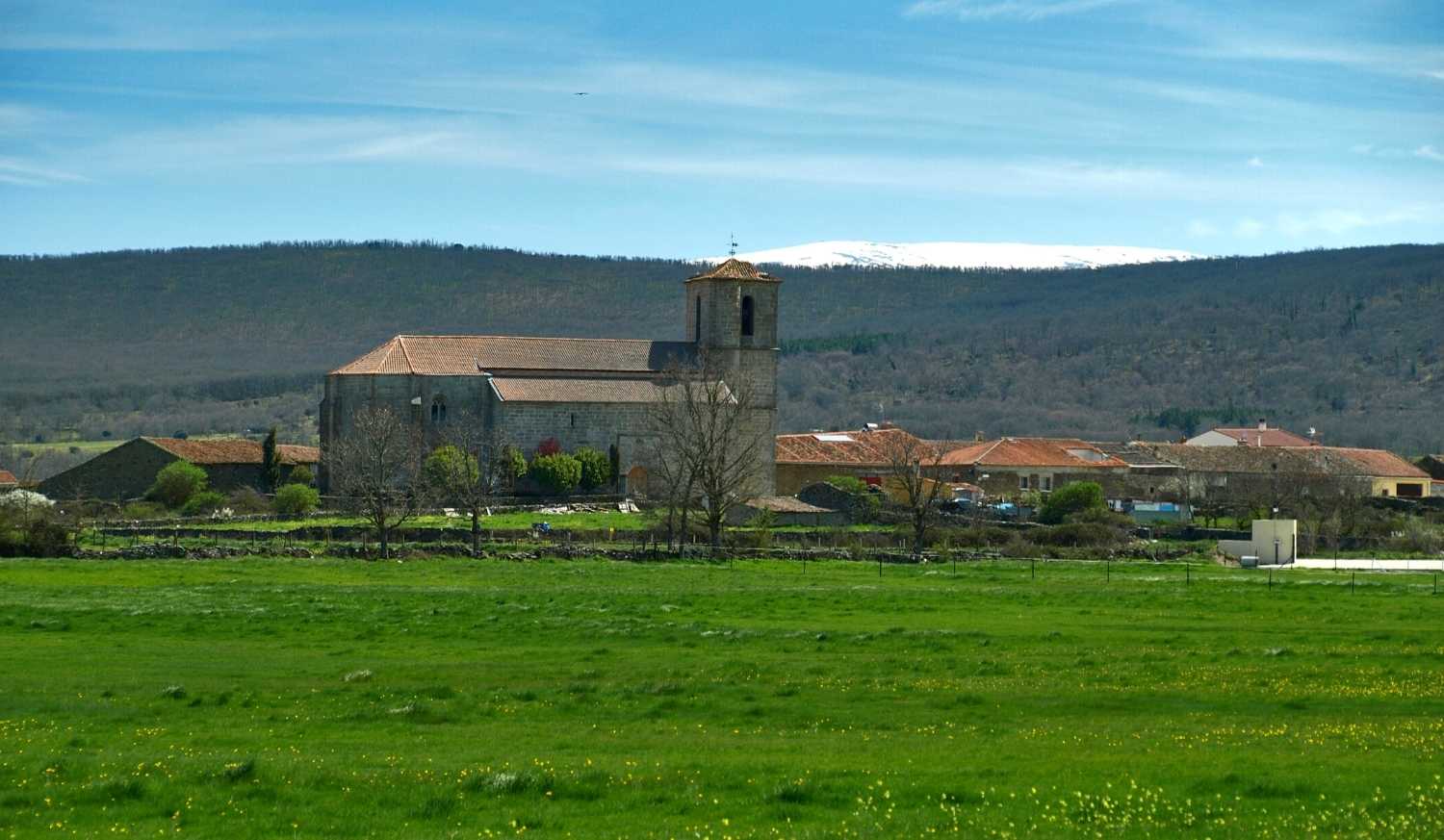 Village of Fuenterroble de Salvatierra with its stone church and green meadows before the snowy sierra, Vía de la Plata.