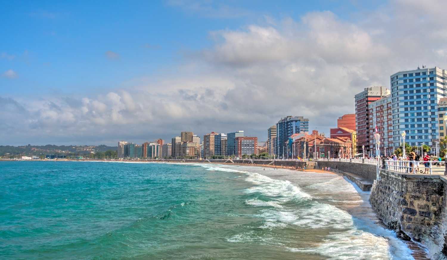 Plage urbaine de Gijón avec des vagues, une promenade en bord de mer et les immeubles sur l'étape de Gijón à Avilés du Chemin du Nord.