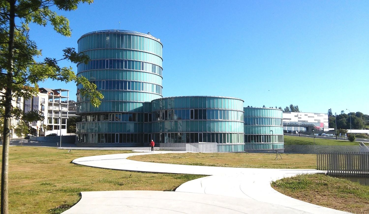 Edificios modernos de vidrio con formas circulares y senderos curvos en el municipio en la etapa de Cea a Lalín del Camino Sanabrés