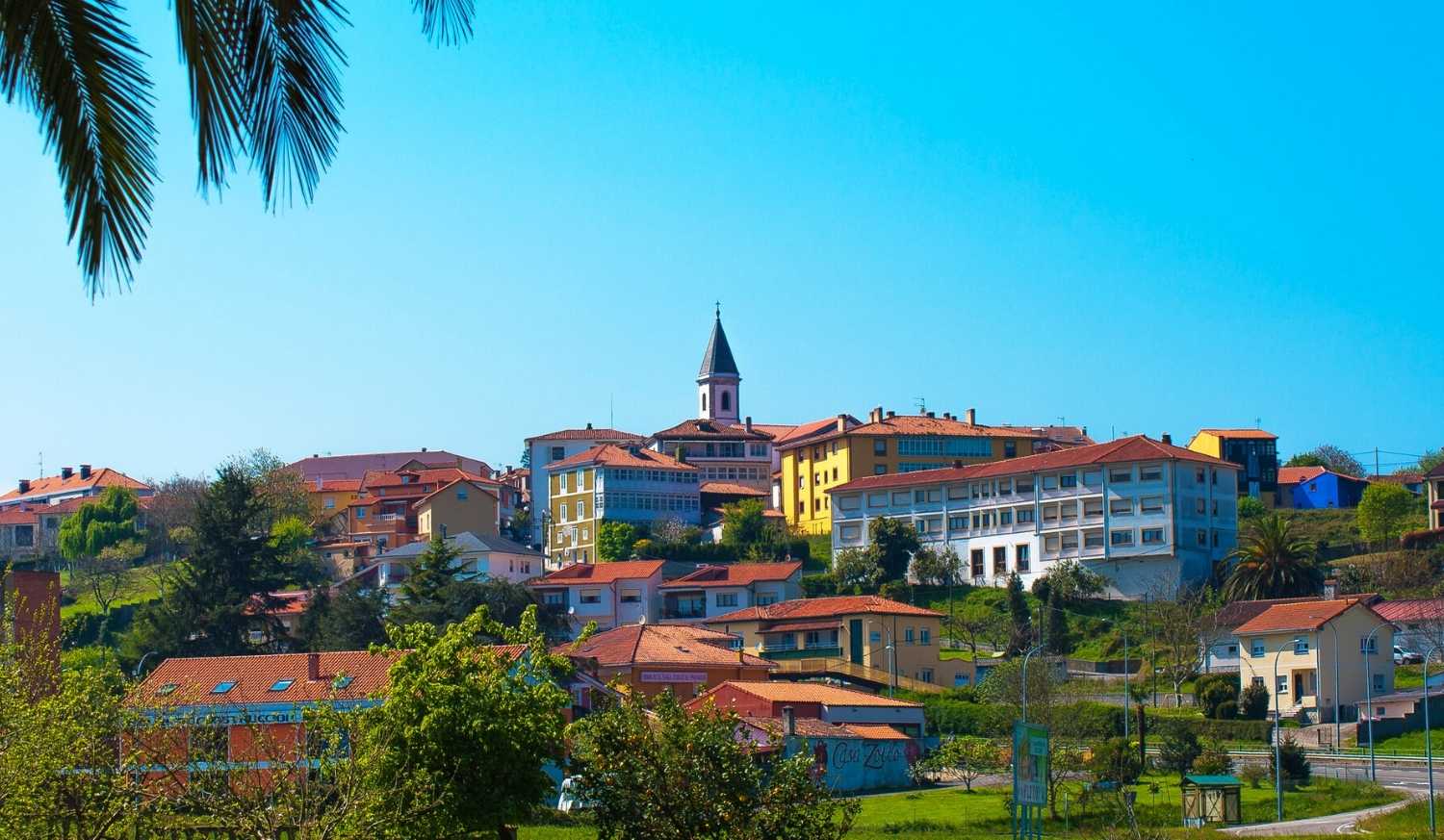 Aldeia de Muros de Nalón na colina com telhados vermelhos e um campanário, meta da etapa do Caminho do Norte desde Avilés.