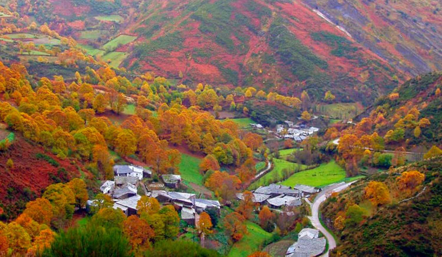 Vista aérea de una aldea en el valle rodeada de laderas otoñales en la etapa de Quiroga a Monforte de Lemos.