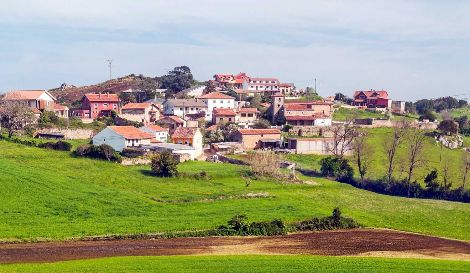 Village sur une butte aux maisons à toits rouges et un clocher parmi les prés sur l'étape de Santander à Santillana del Mar du Chemin du Nord.