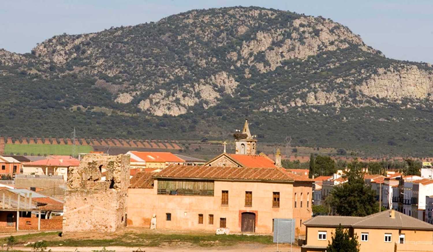 Pueblo con iglesia de ladrillo y torre en ruinas al pie de una gran montaña, etapa de Torremejía a Mérida.