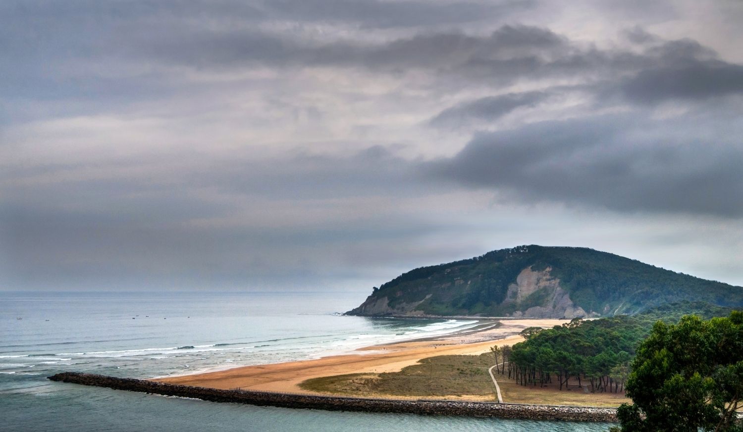 A wide beach and estuary with a green headland under cloudy skies on the Villaviciosa to Gijón stage of the Camino del Norte