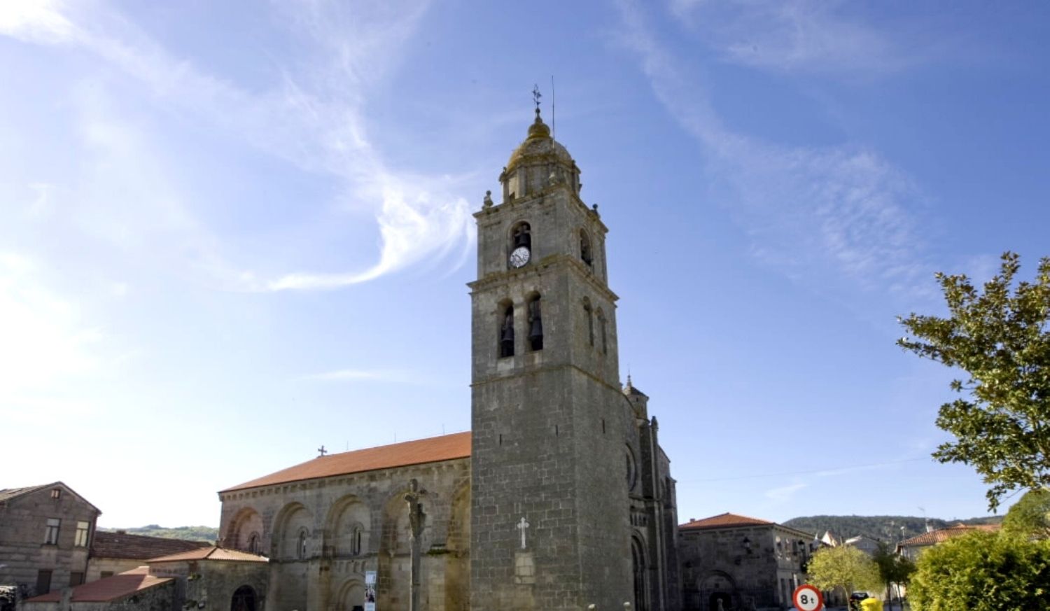 Imponente iglesia colegiata románica con alta torre y un cruceiro delante en Xunqueira de Ambía, etapa de Laza a Xunqueira de Ambía.